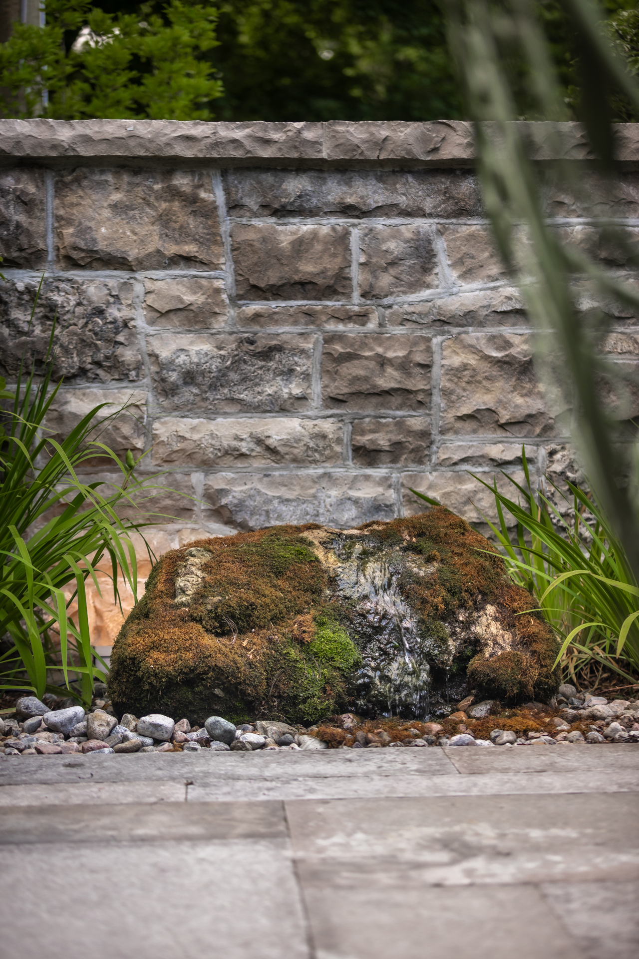 Moss-covered boulder bubbler beside a stone wall