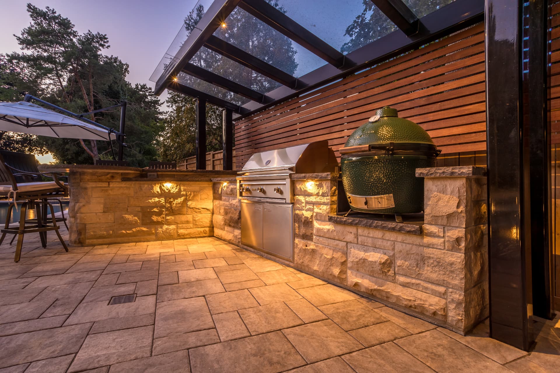 Stone outdoor kitchen with grill and Big Green Egg under a glass pergola
