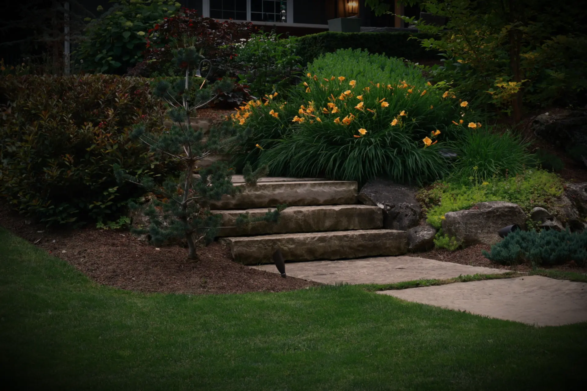 Natural stone steps rising through a lit perennial garden
