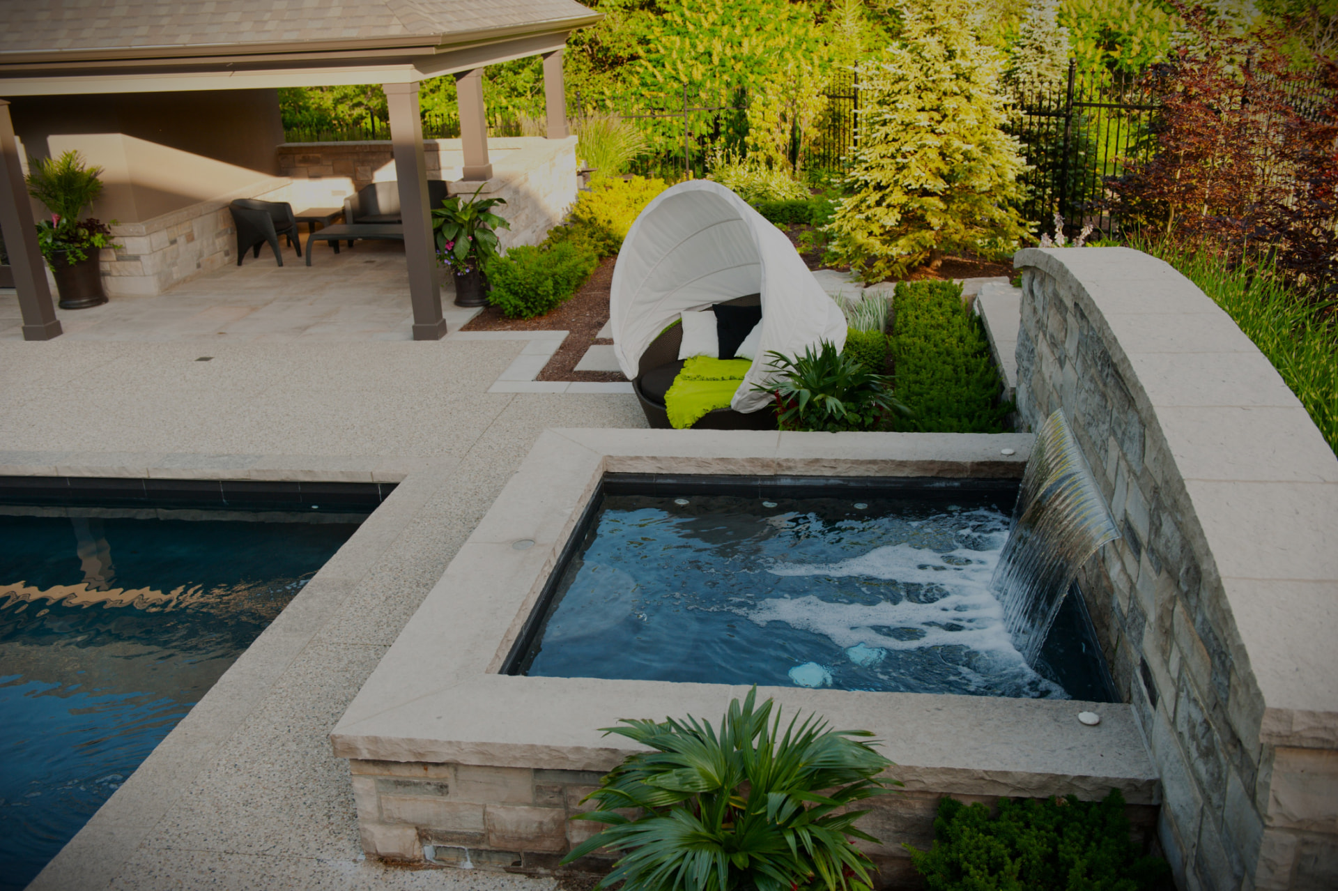 Raised spa with sheer spillway beside the pool
