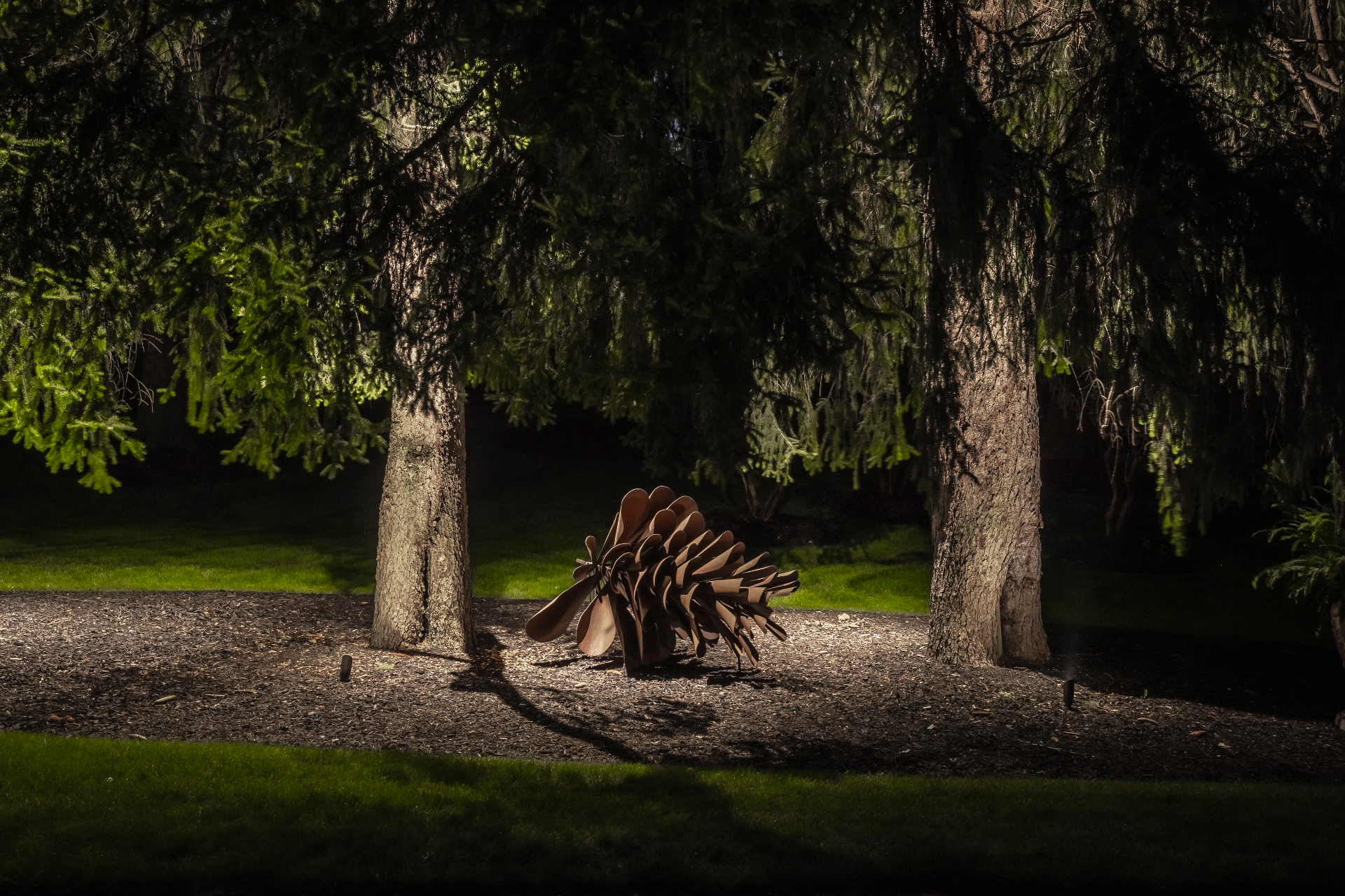 Uplit pinecone sculpture beneath mature trees