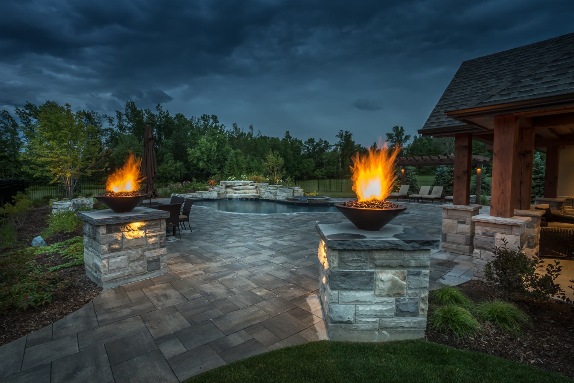 Paired fire bowls atop stone pillars framing the pool